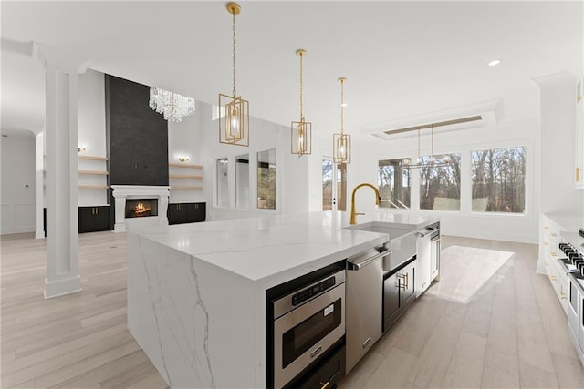 kitchen with light stone counters, a center island with sink, appliances with stainless steel finishes, pendant lighting, and a fireplace