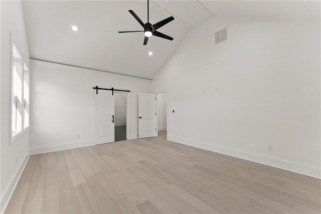 empty room featuring a barn door, a wealth of natural light, high vaulted ceiling, and light hardwood / wood-style flooring