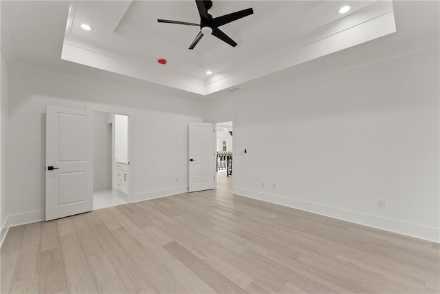 empty room featuring ornamental molding, light hardwood / wood-style flooring, ceiling fan, and a tray ceiling