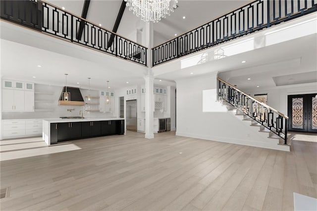 unfurnished living room featuring a chandelier, decorative columns, light hardwood / wood-style flooring, and a high ceiling