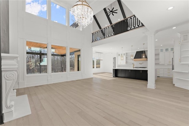 unfurnished living room featuring an inviting chandelier, a towering ceiling, light hardwood / wood-style floors, and ornate columns