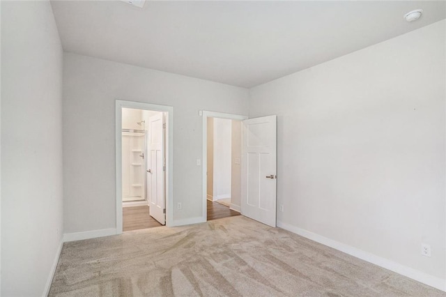 unfurnished bedroom featuring a walk in closet, light colored carpet, and ensuite bathroom