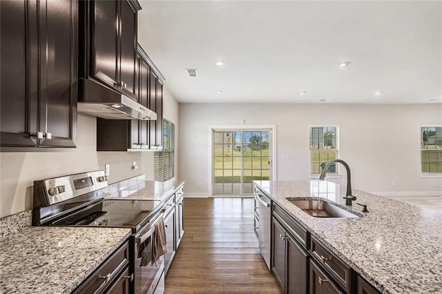 kitchen with appliances with stainless steel finishes, dark hardwood / wood-style flooring, light stone counters, dark brown cabinets, and sink