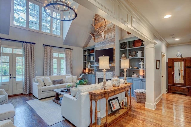 living room featuring an inviting chandelier, built in features, light hardwood / wood-style flooring, and french doors