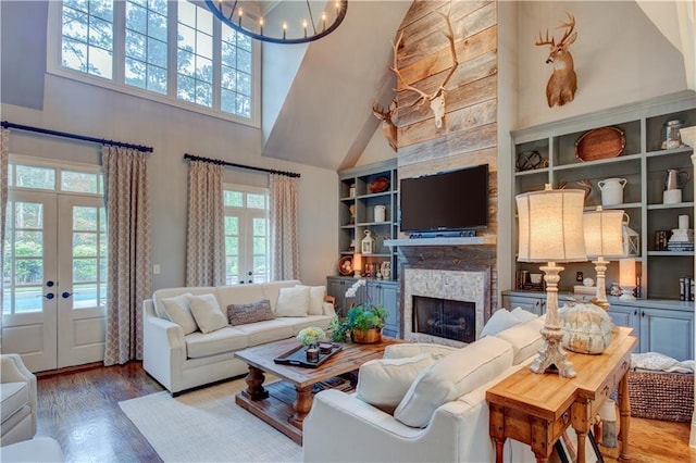 living room with high vaulted ceiling, an inviting chandelier, french doors, a fireplace, and wood-type flooring