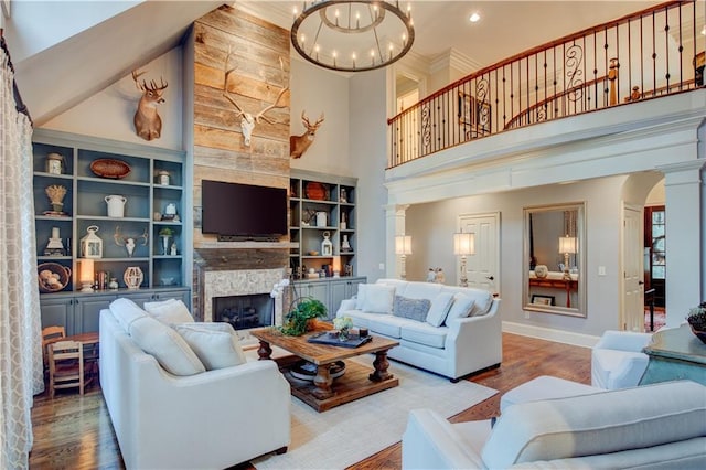 living room with built in shelves, an inviting chandelier, a stone fireplace, a towering ceiling, and hardwood / wood-style flooring