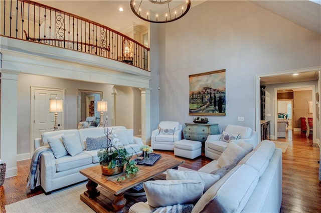 living room with ornate columns, hardwood / wood-style floors, a towering ceiling, and a chandelier