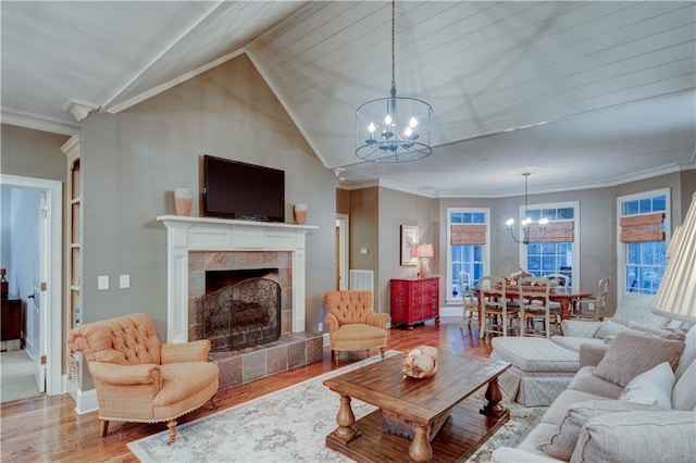 living room featuring hardwood / wood-style floors, a notable chandelier, crown molding, and a tiled fireplace