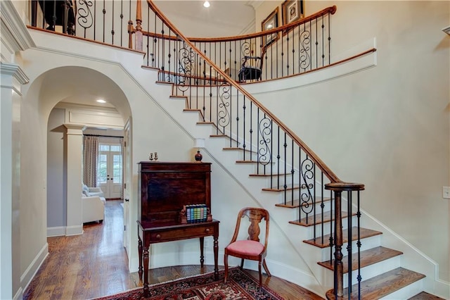 staircase featuring wood-type flooring, french doors, crown molding, and a high ceiling