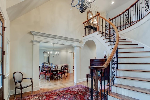 stairway with hardwood / wood-style flooring, ornate columns, ornamental molding, and a chandelier