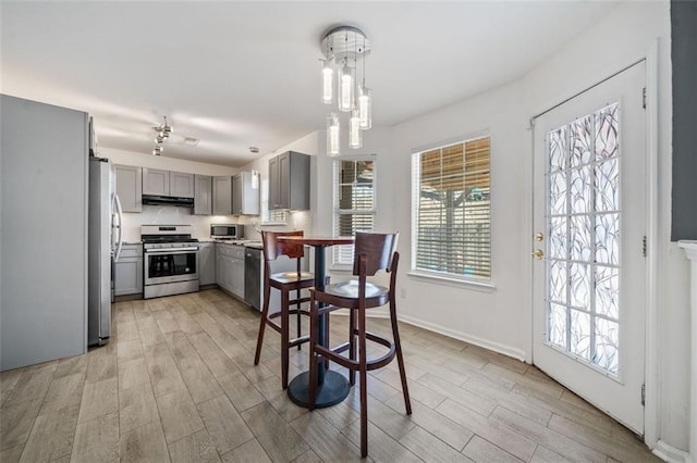 kitchen with light hardwood / wood-style flooring, gray cabinets, appliances with stainless steel finishes, backsplash, and decorative light fixtures