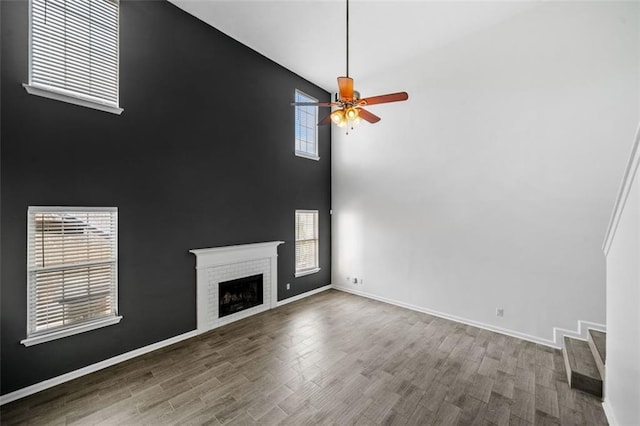 unfurnished living room featuring ceiling fan, dark hardwood / wood-style flooring, a brick fireplace, and a high ceiling