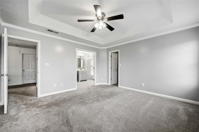 unfurnished bedroom featuring light carpet, ensuite bath, ornamental molding, and a raised ceiling