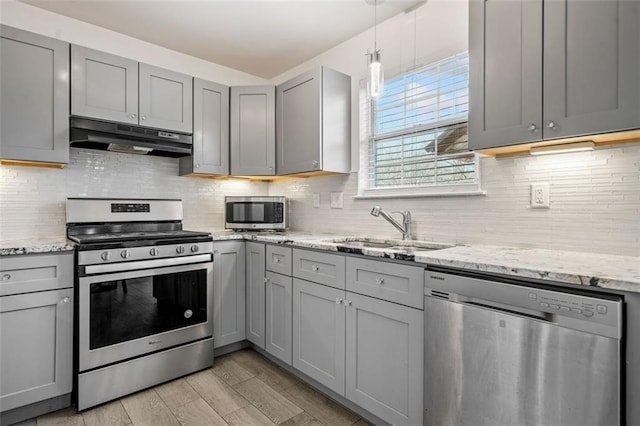 kitchen featuring sink, gray cabinetry, decorative backsplash, light stone counters, and stainless steel appliances