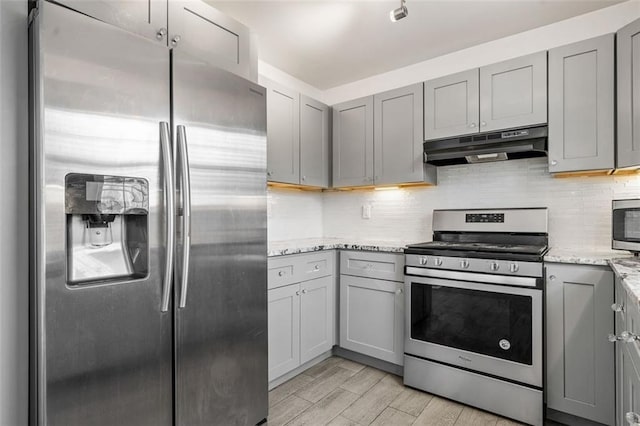 kitchen featuring gray cabinetry, light stone counters, stainless steel appliances, light hardwood / wood-style floors, and decorative backsplash