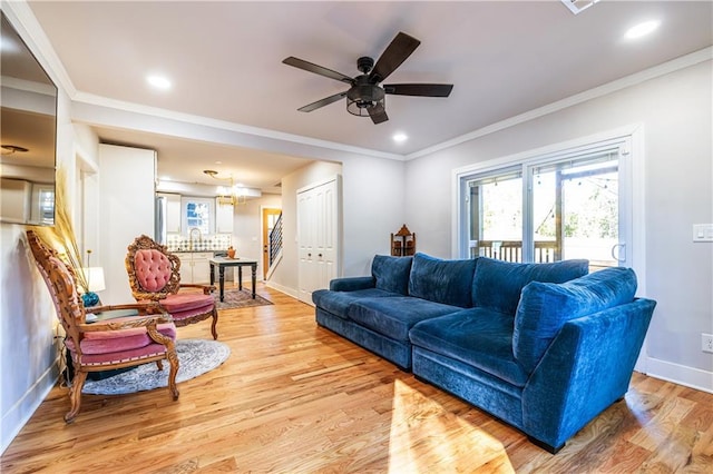 living room featuring crown molding, light hardwood / wood-style floors, and ceiling fan with notable chandelier