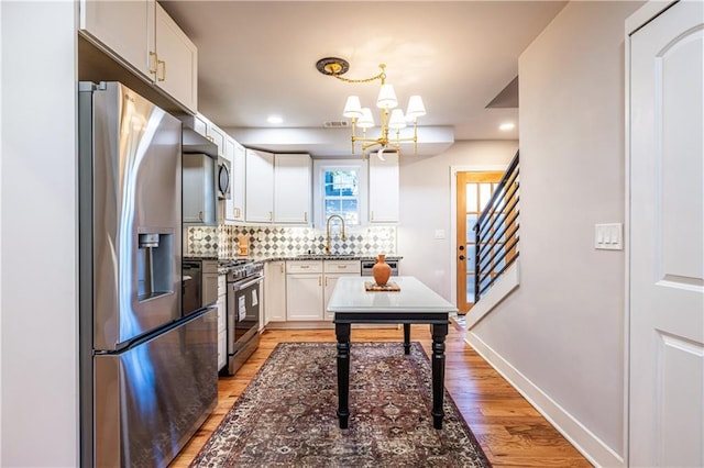 kitchen featuring appliances with stainless steel finishes, backsplash, decorative light fixtures, a notable chandelier, and white cabinets