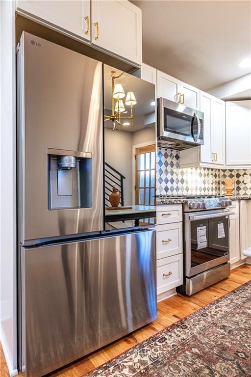 kitchen featuring decorative backsplash, appliances with stainless steel finishes, an inviting chandelier, white cabinets, and light hardwood / wood-style floors