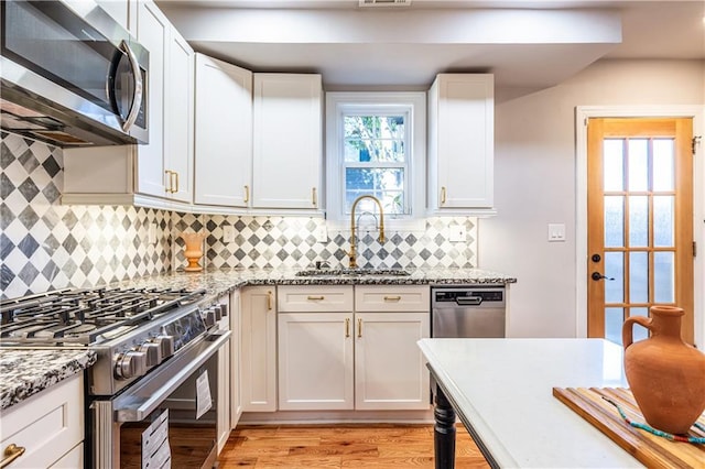 kitchen with sink, tasteful backsplash, light stone counters, white cabinetry, and stainless steel appliances