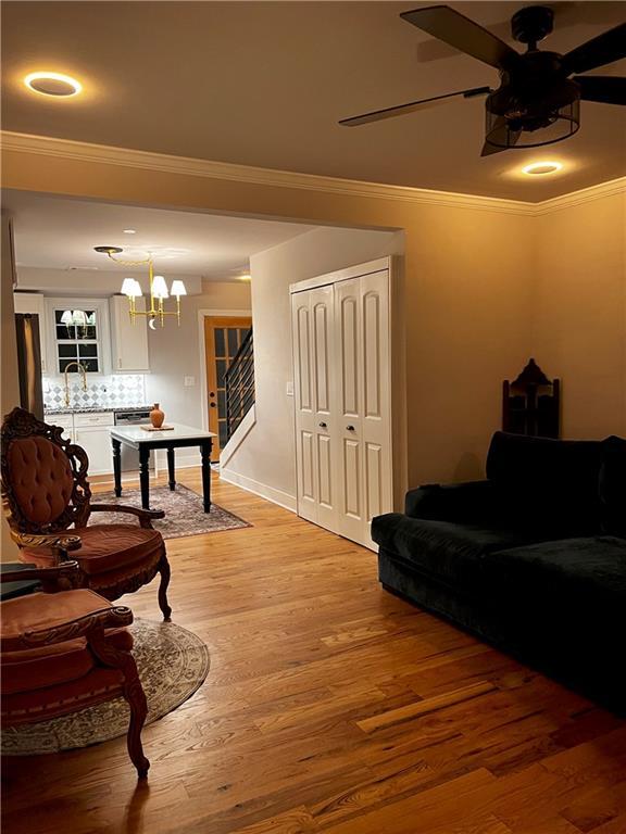 living room with hardwood / wood-style floors, ceiling fan with notable chandelier, and crown molding