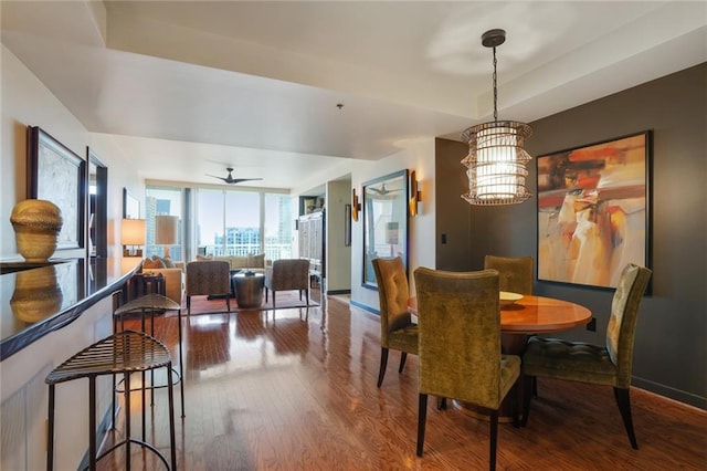 dining room featuring an inviting chandelier, a raised ceiling, wood finished floors, and baseboards
