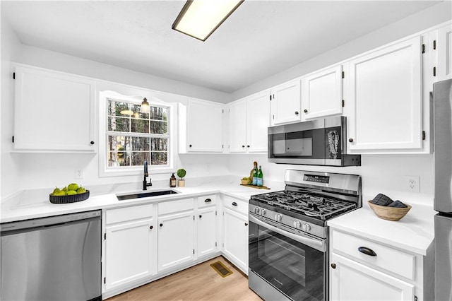 kitchen with a sink, light wood-style floors, white cabinets, light countertops, and appliances with stainless steel finishes