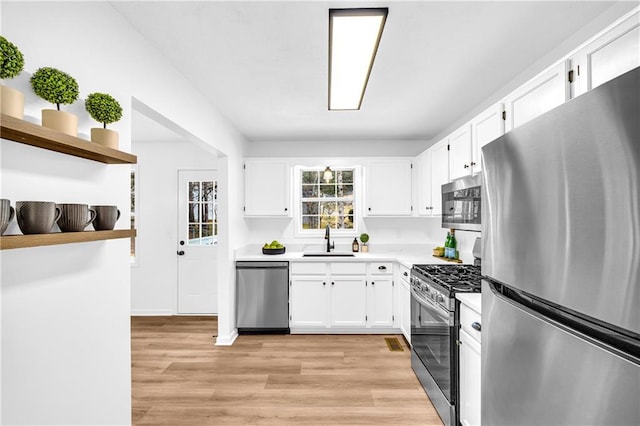 kitchen featuring stainless steel appliances, a sink, white cabinetry, light countertops, and open shelves