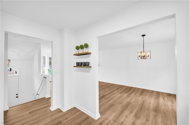 hall with light wood-style floors, baseboards, a notable chandelier, and an upstairs landing