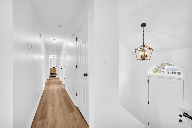 hall featuring light wood-style floors, a notable chandelier, and baseboards