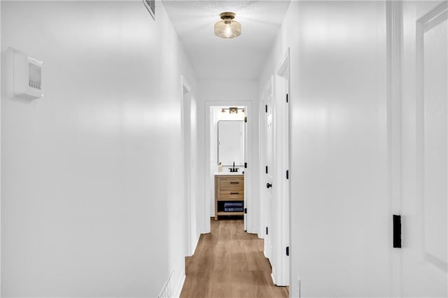 corridor with light wood finished floors, a sink, and visible vents