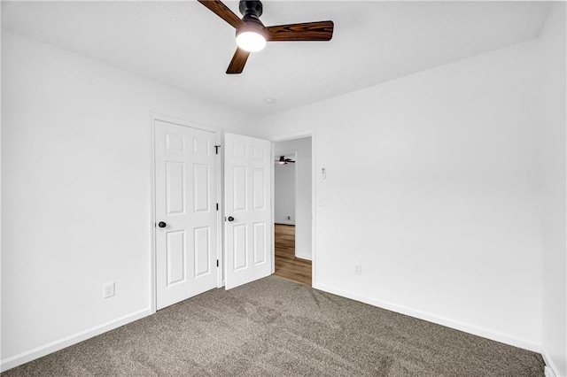 unfurnished bedroom with a ceiling fan, dark colored carpet, and baseboards