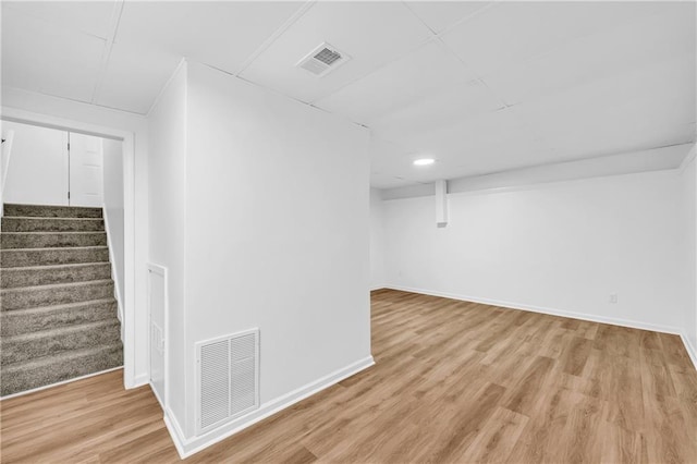 finished basement featuring stairs, light wood finished floors, visible vents, and baseboards