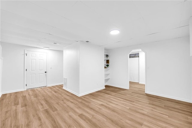 basement with light wood-type flooring, baseboards, and arched walkways