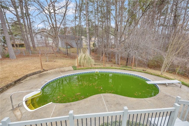 view of swimming pool with fence and a diving board