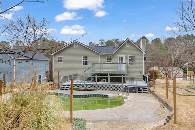 rear view of house with a chimney, an outdoor pool, and a deck