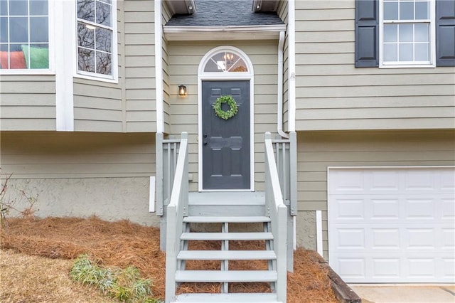 view of exterior entry featuring roof with shingles and an attached garage