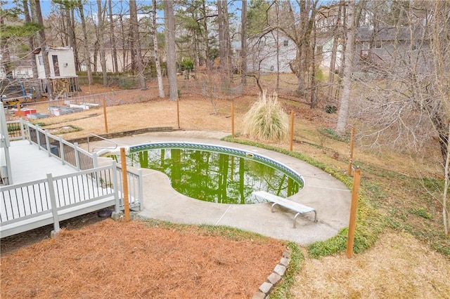 outdoor pool with a deck, fence, and a diving board