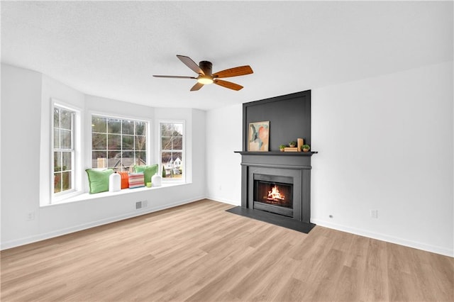 unfurnished living room with a large fireplace, baseboards, visible vents, and light wood finished floors