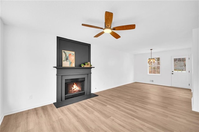 unfurnished living room with light wood finished floors, a fireplace with flush hearth, a ceiling fan, and baseboards