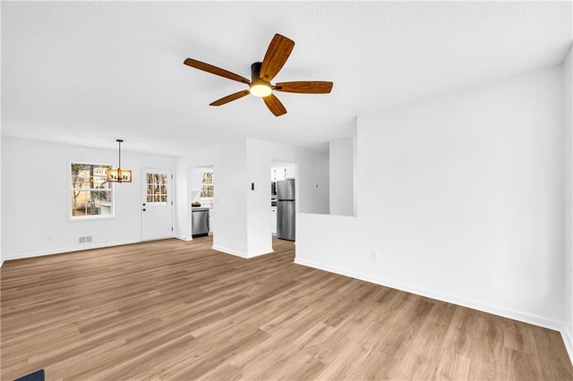 unfurnished living room with light wood-type flooring, visible vents, baseboards, and ceiling fan with notable chandelier