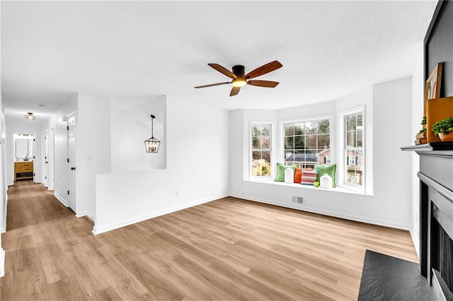 unfurnished living room featuring light wood-type flooring, a fireplace with flush hearth, a ceiling fan, and baseboards