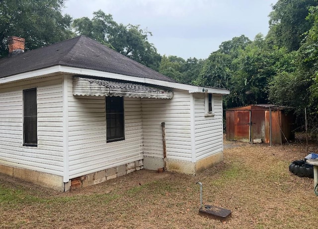 view of property exterior with a shed, a shingled roof, and an outbuilding