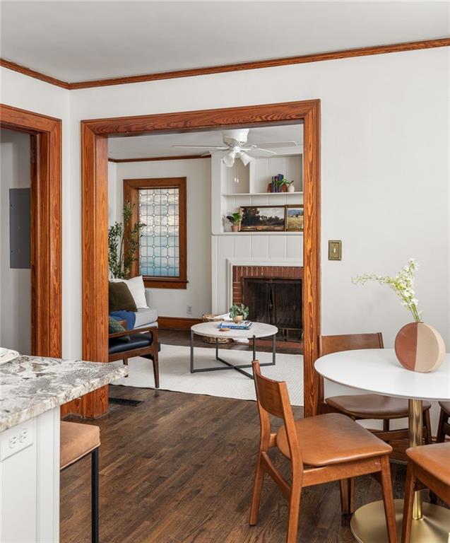 dining area featuring ceiling fan, a fireplace, wood finished floors, ornamental molding, and electric panel