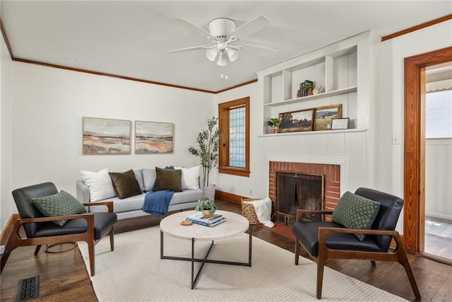 sitting room with a brick fireplace, visible vents, crown molding, and wood finished floors