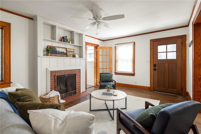 living room with baseboards, ceiling fan, ornamental molding, wood finished floors, and a brick fireplace