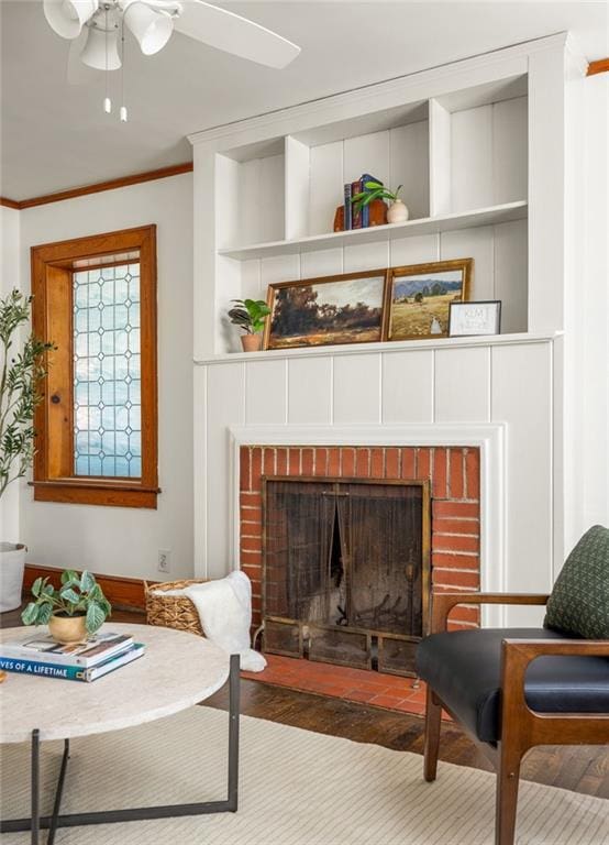 living area with ornamental molding, a brick fireplace, wood finished floors, and built in shelves