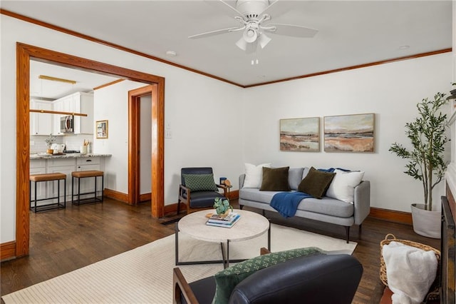 living area with ornamental molding, dark wood finished floors, a ceiling fan, and baseboards