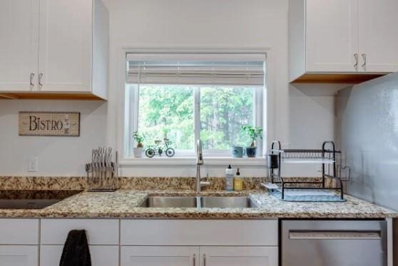 kitchen featuring stainless steel dishwasher, light stone counters, white cabinetry, and sink