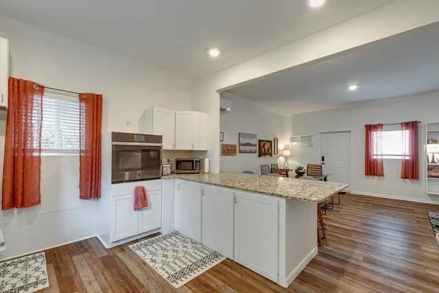 kitchen featuring a breakfast bar, white cabinets, dark hardwood / wood-style floors, appliances with stainless steel finishes, and kitchen peninsula