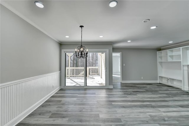 unfurnished living room featuring a chandelier, a wainscoted wall, crown molding, and wood finished floors